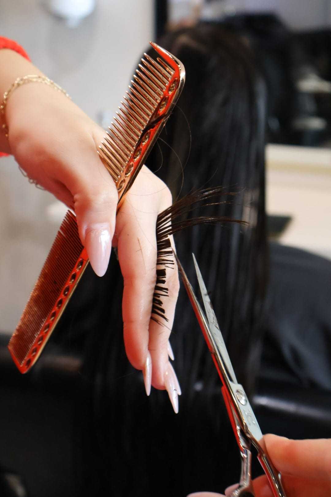 Hairdresser trims long black hair with scissors and comb in a salon.